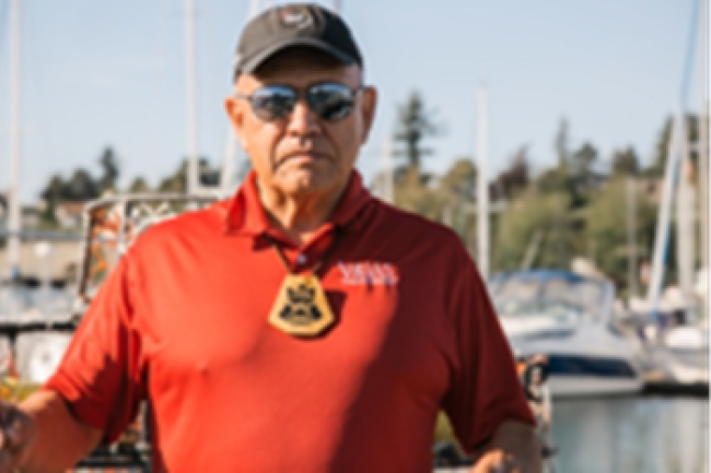 Darrell standing in front of boats at the Marina, with a red shirt and black hat on